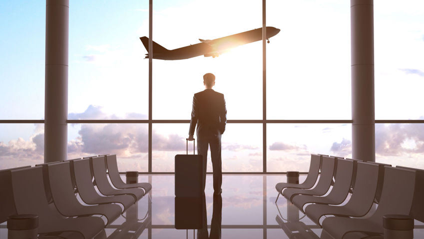 Image of a business person looking out of an airport window at a plane taking off